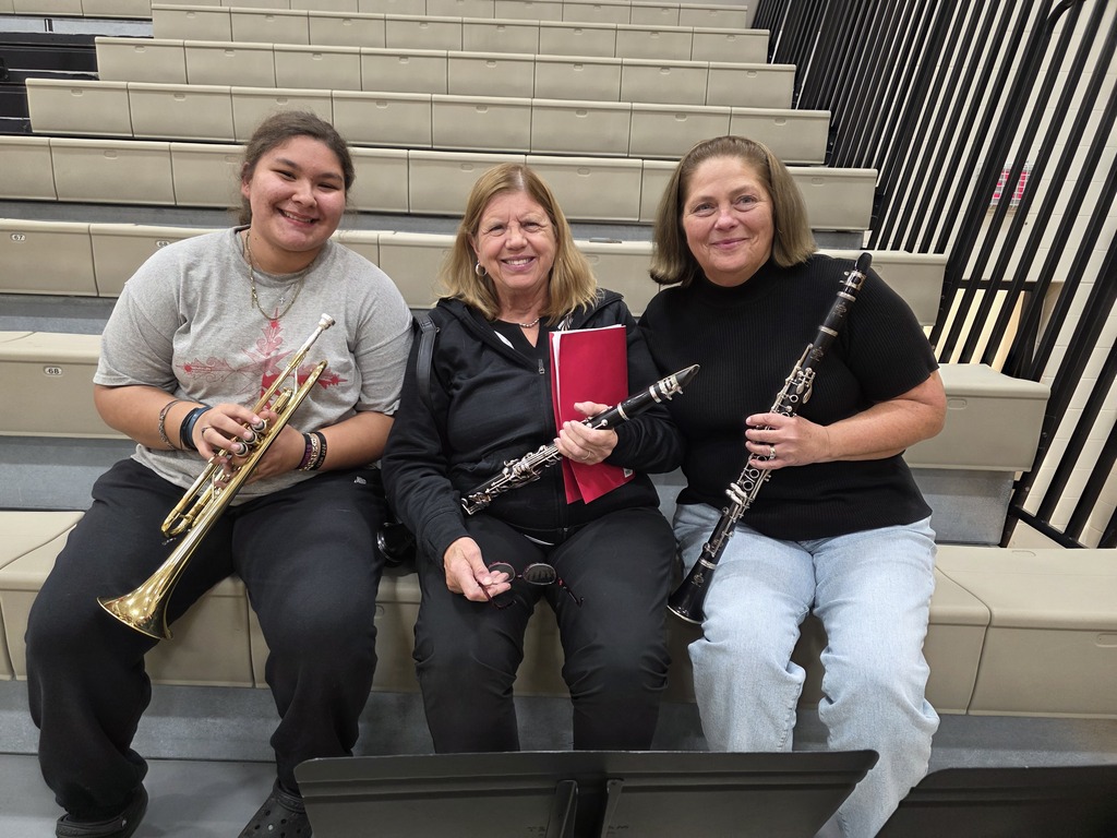 Three women holding instruments sitting on bleachers