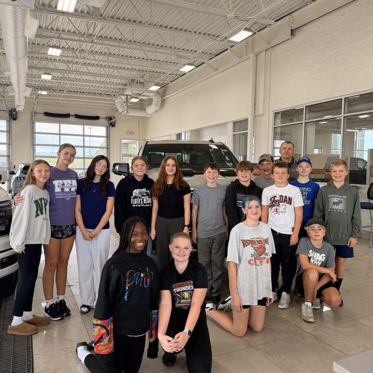 students posing for picture in front of car on display at dealership