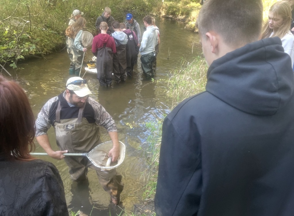 Students watching man in stream with fish in net