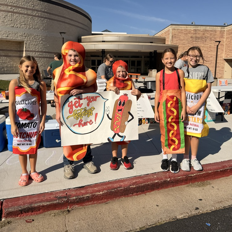 students I. front of high school wearing hotdog costumes and holding a banner “get your hot dogs here” 