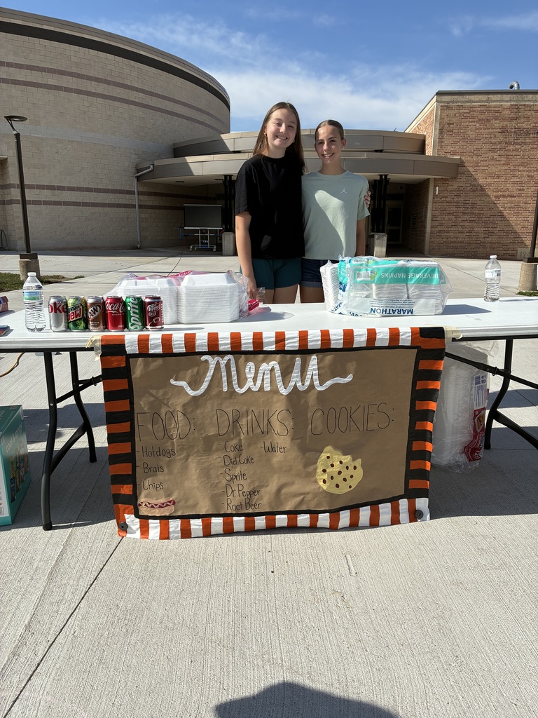Two students standing behind table with a sign that says Menu