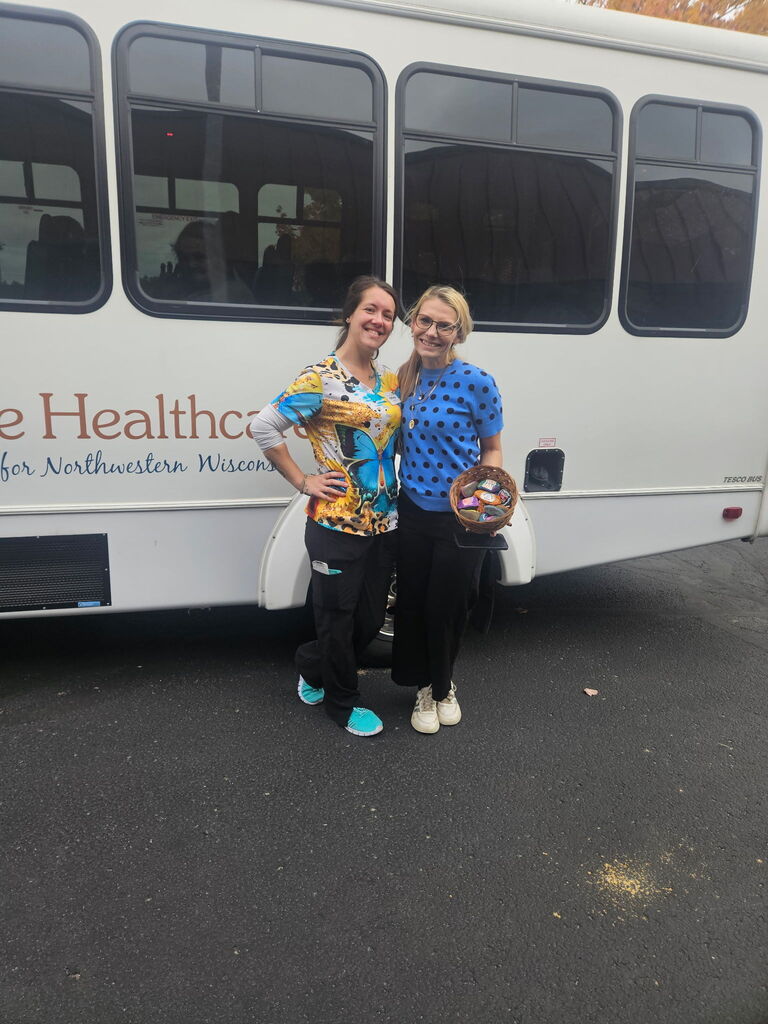 Image description for accessibility:  Two women in front of a bus  holding a basket of painted rocks