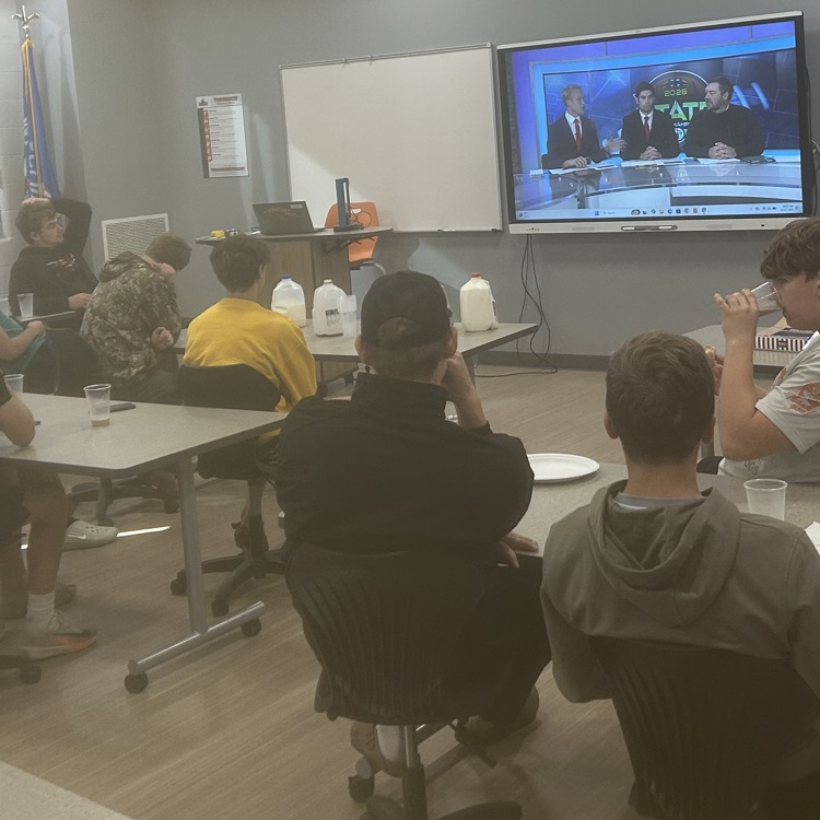 Image description for accessibility: Football Players watching playoff announcement on big screen