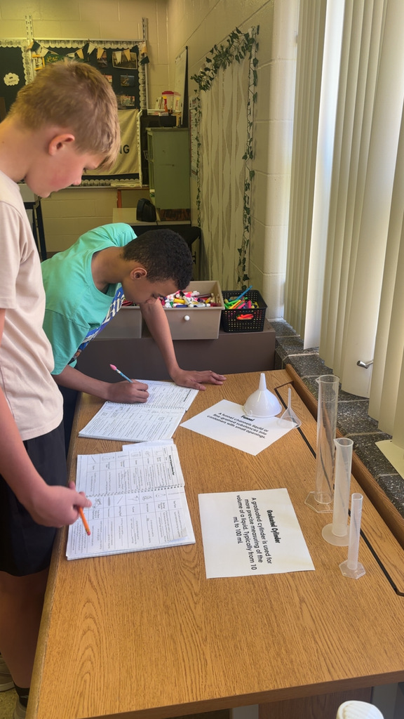 Image Description for accessibility: Students looking a science equipment and writing in notebooks