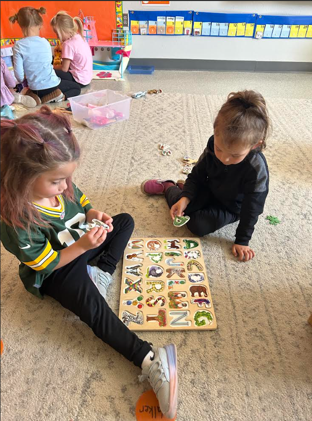 Image Description for accessibility: Students sitting on floor doing a wooden ABC puzzle