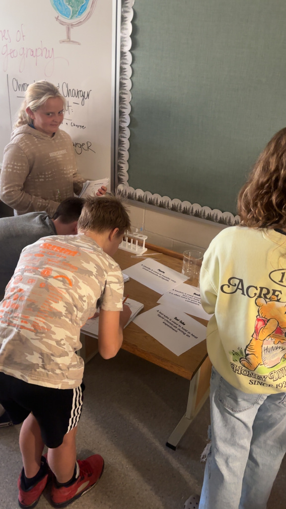 Image Description for accessibility: Students looking a science equipment and writing in notebooks