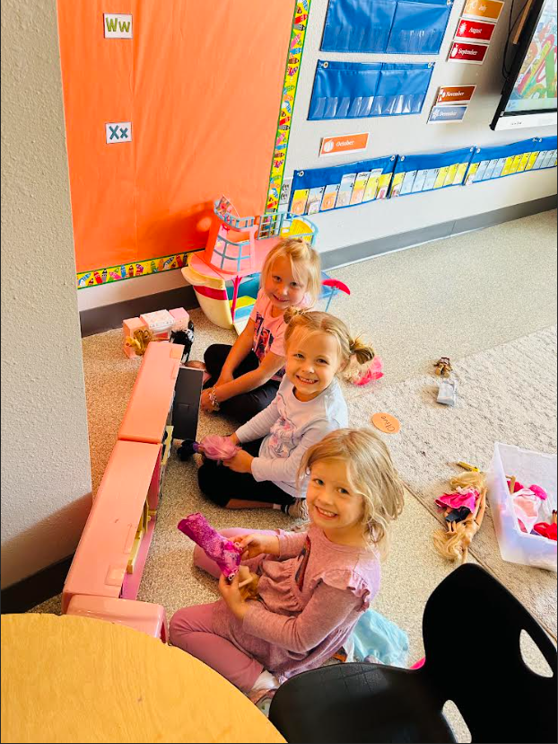 Image Description for accessibility: Students playing together with Barbie Dolls