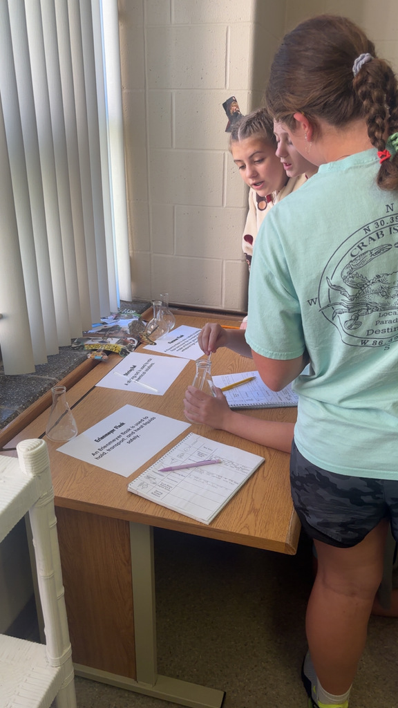 Image Description for accessibility: Students looking a science equipment and writing in notebooks