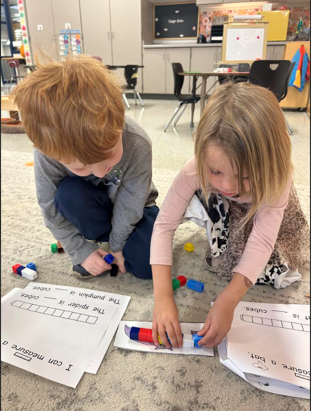Image Description for accessibility: Students sitting on the floor using cubes to measure