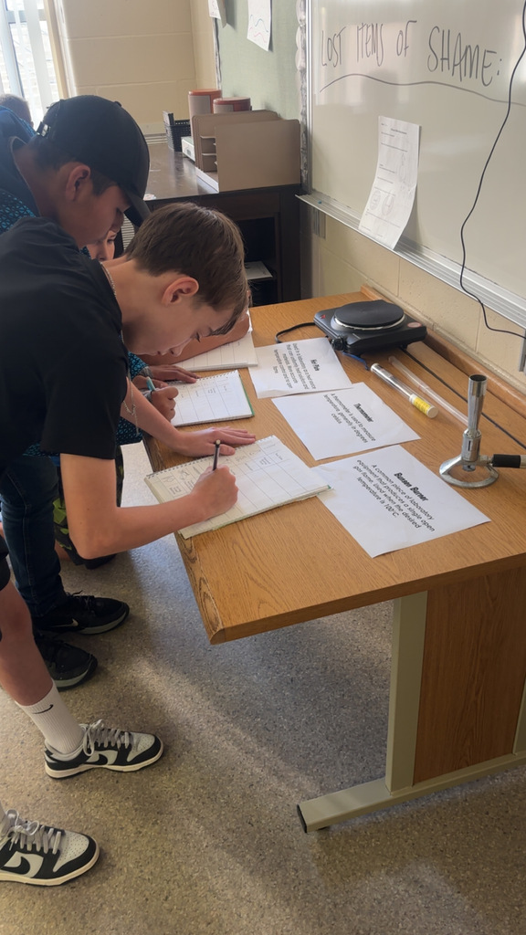 Image Description for accessibility: Students looking a science equipment and writing in notebooks