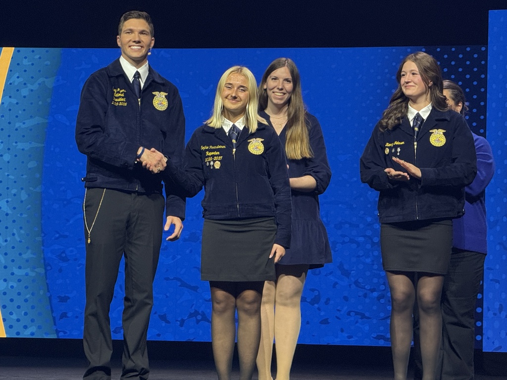 Image Description for accessibility:  Sophis on stage with four others.  Shaking hands