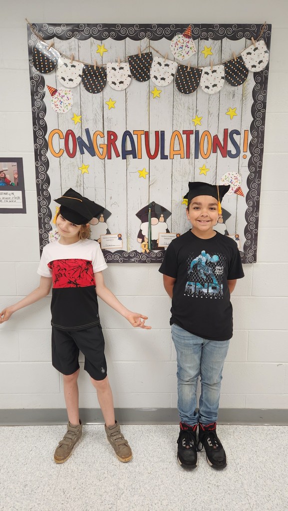 Two students posing inside with their graduation caps