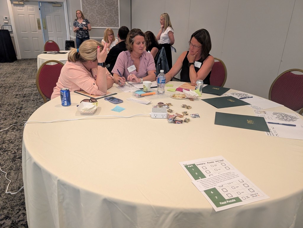 Three people at a table working together and more people in the background