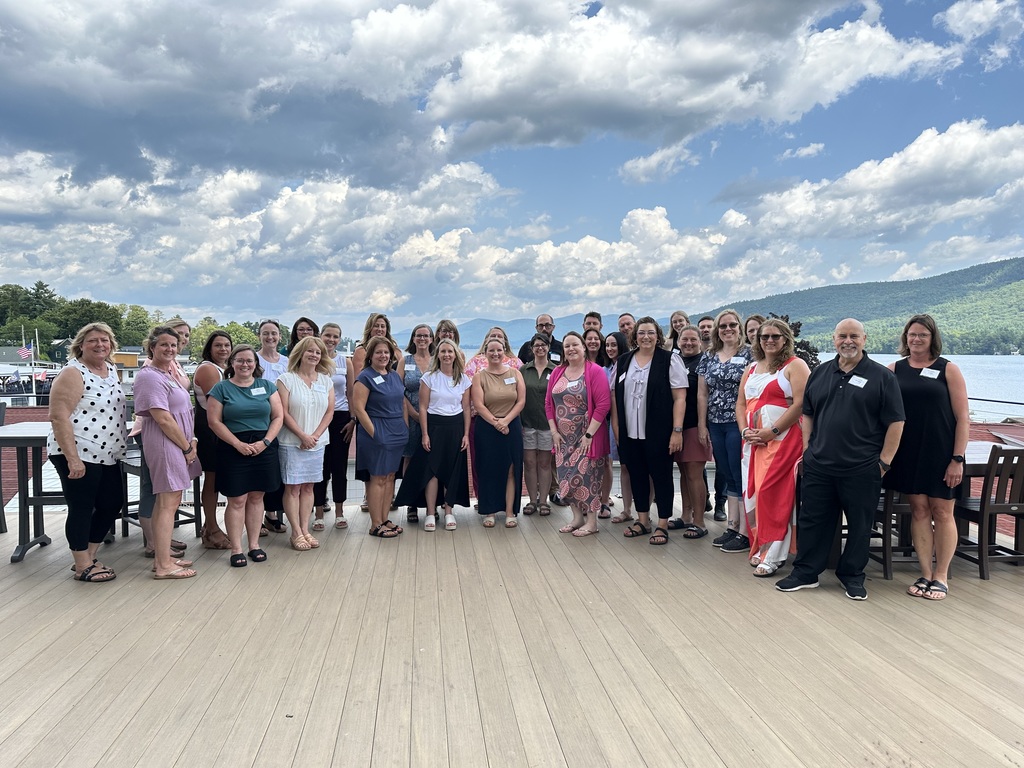 Large group of educators standing on a dock with mountains and sky behind them