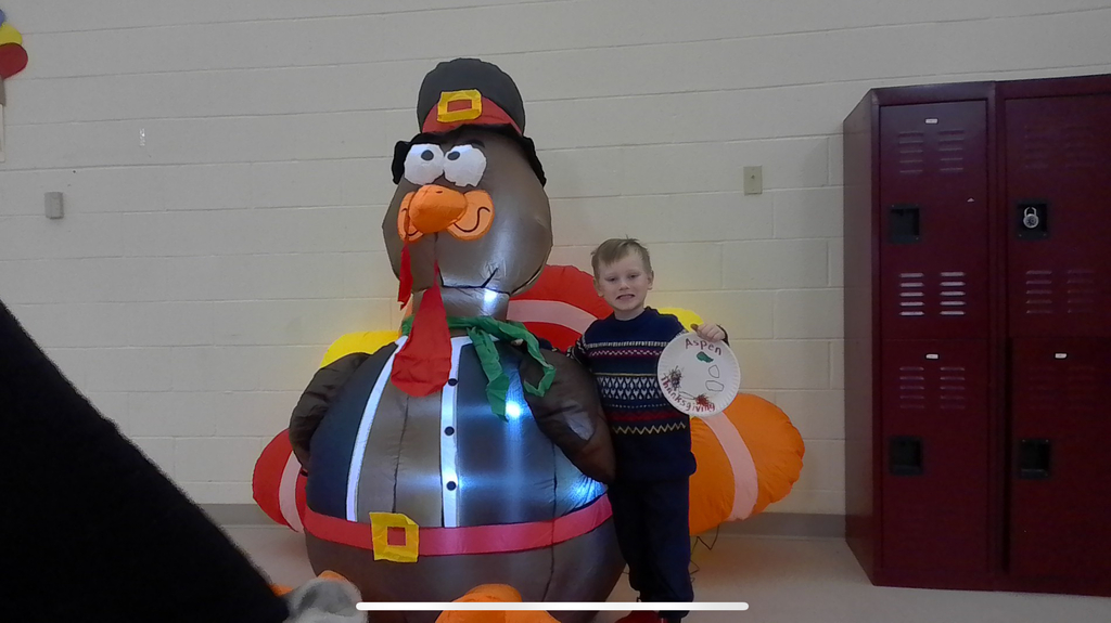 Elementary student holding a drawing of his thanksgiving standing with an inflatable turkey.