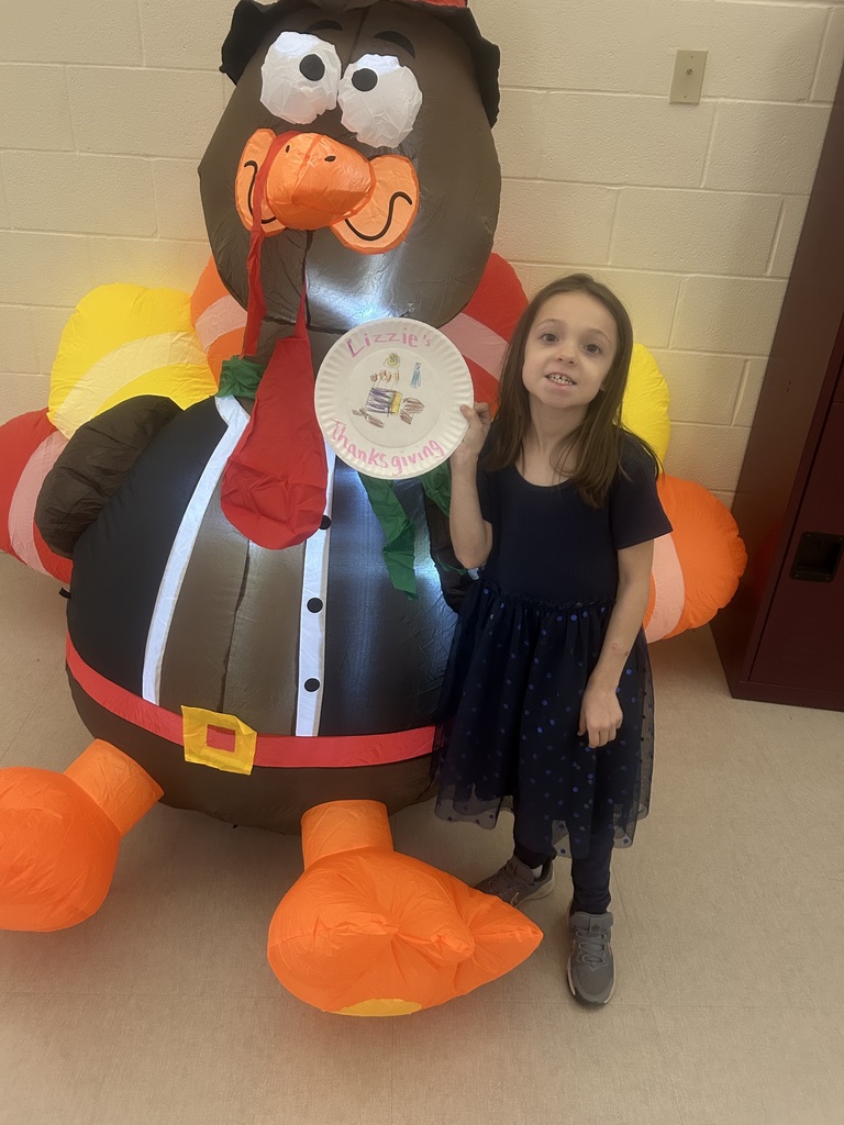 Elementary student holding a drawing of her thanksgiving standing with an inflatable turkey.
