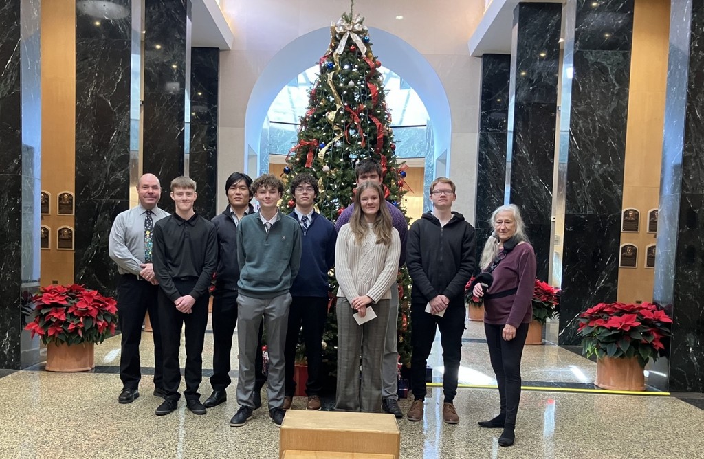 Students, instructor, and tour guide standing in front of a decorated christmas tree at the baseball hall of fame