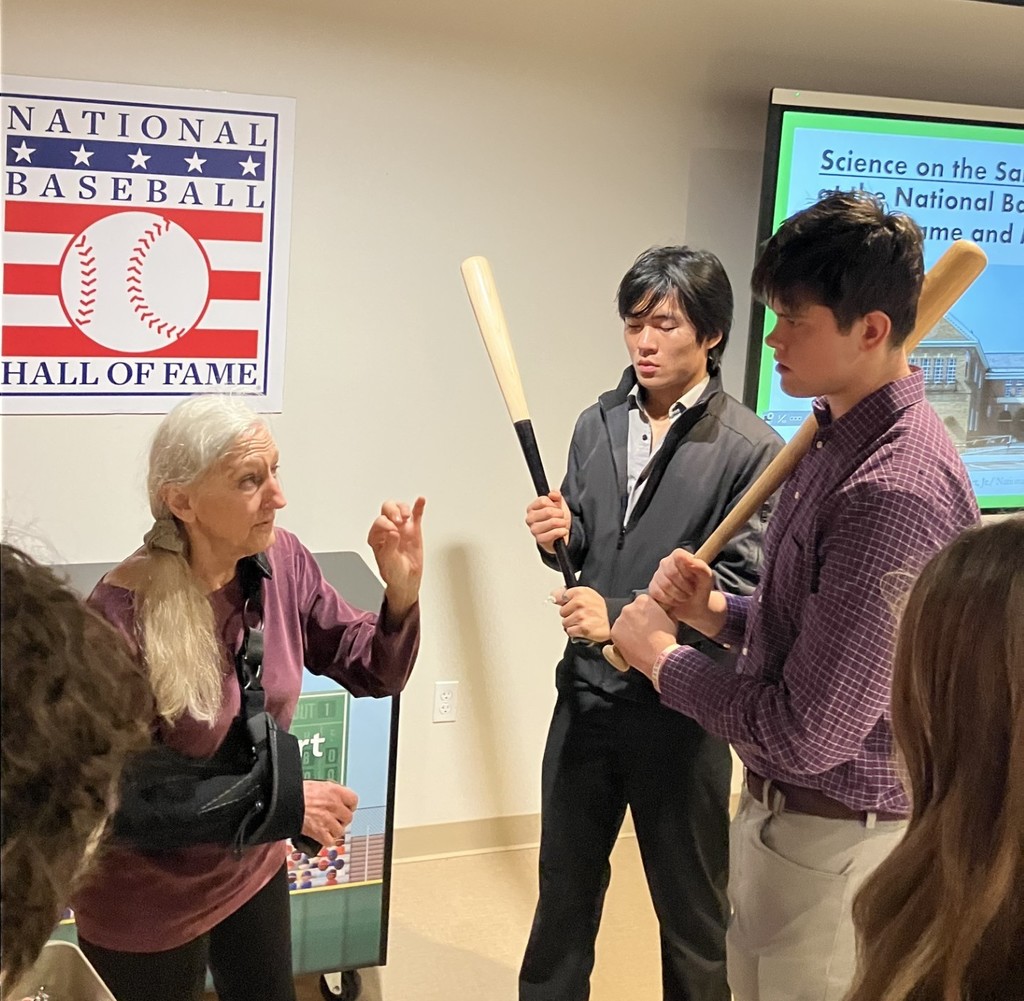 Two students holding baseball bats while the tour guide speaks