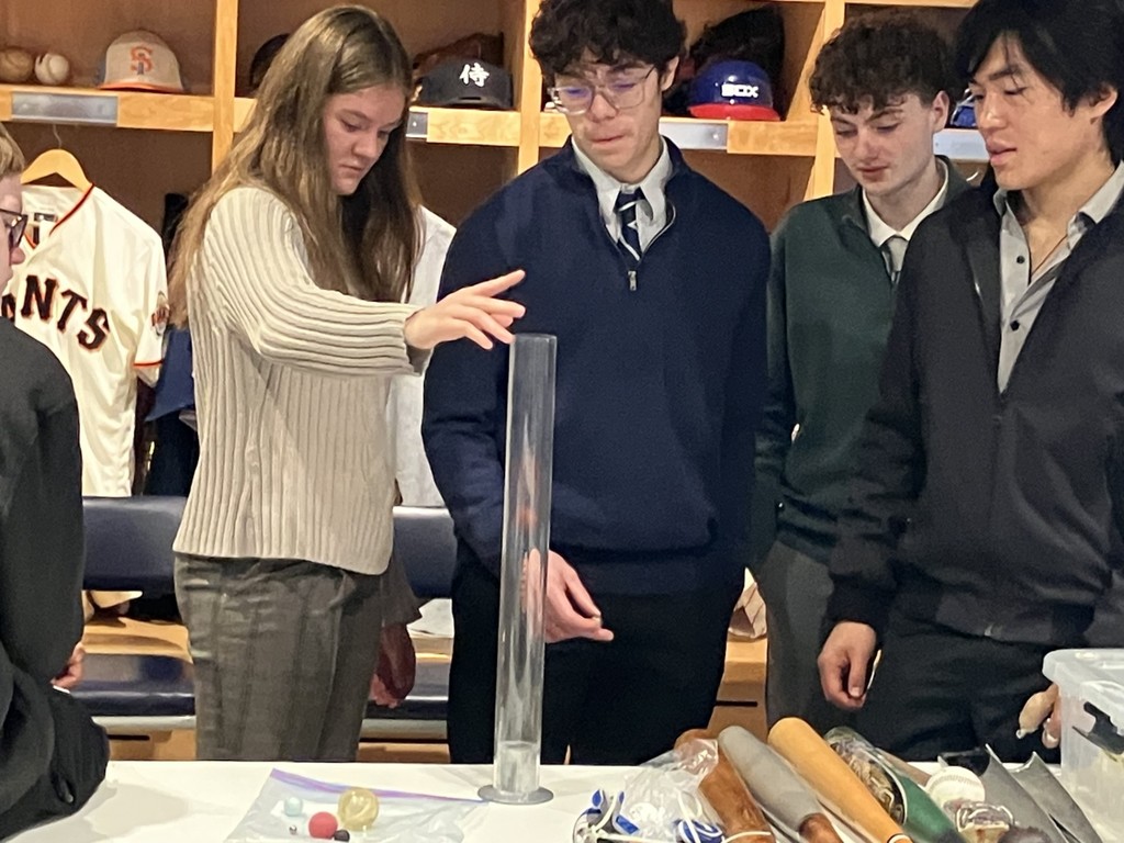 Four students gathered around a table with a tube doing an experiment