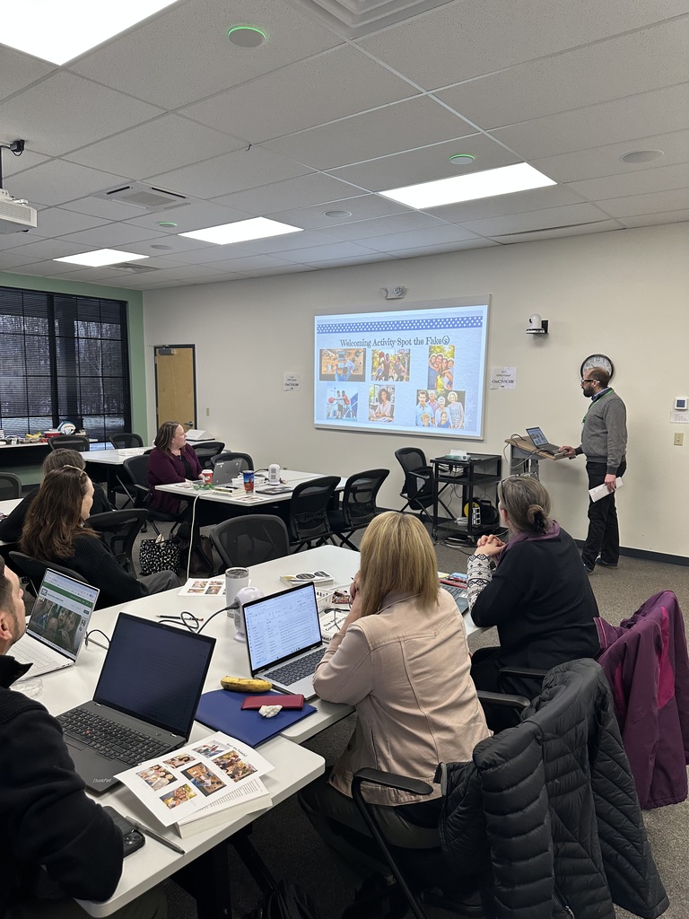 An Instructional Support Staff member leading a training with a group of people sitting at tables.