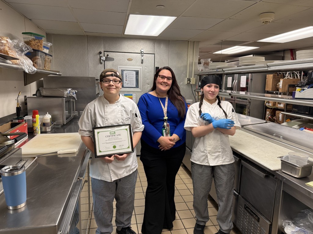 Two students with their culinary arts instructor in a restaurant kitchen
