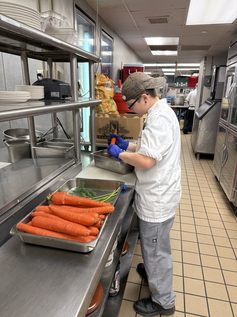Student in a restaurant kitchen preparing carrots