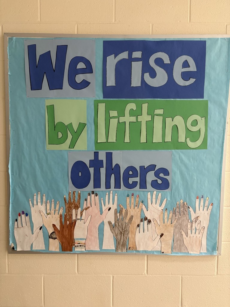 A bulletin board that with handprints that says We rise by lifting others