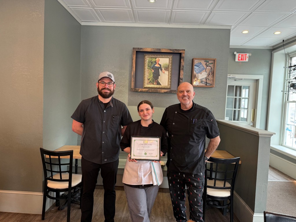 Student holding certificate with two restaurant employees