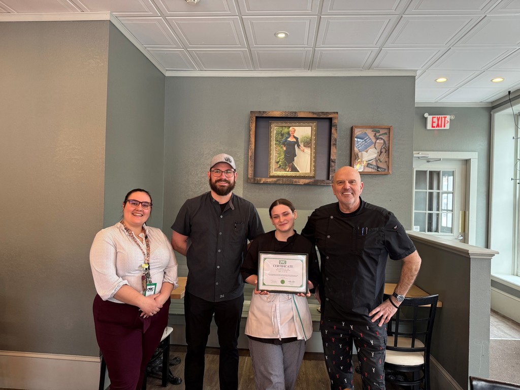 Student holding certificate with two restaurant employees and culinary instructor