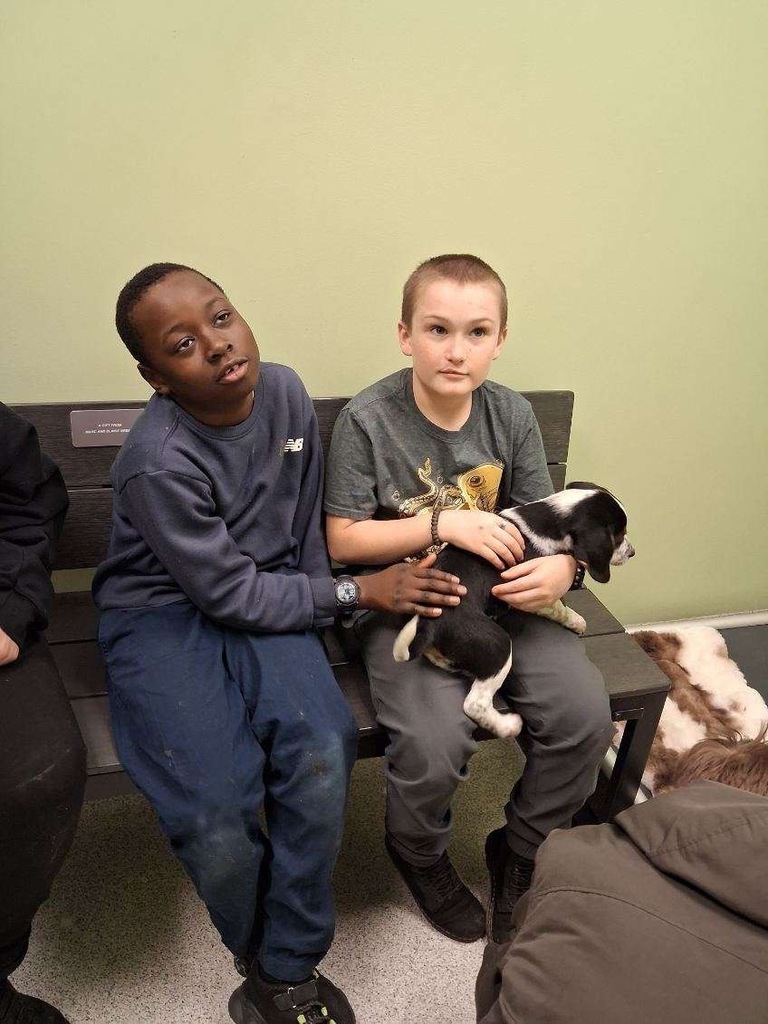 Two students - one holding a puppy in his lap and the other petting the puppy