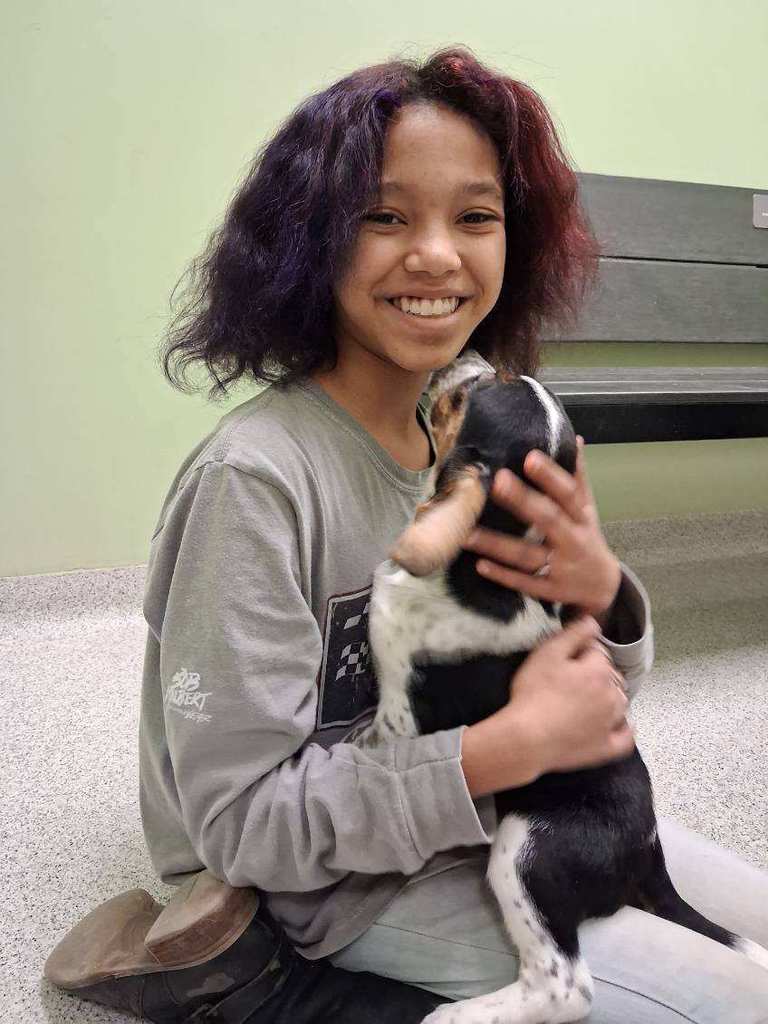 Student holding a brown and white puppy and smiling