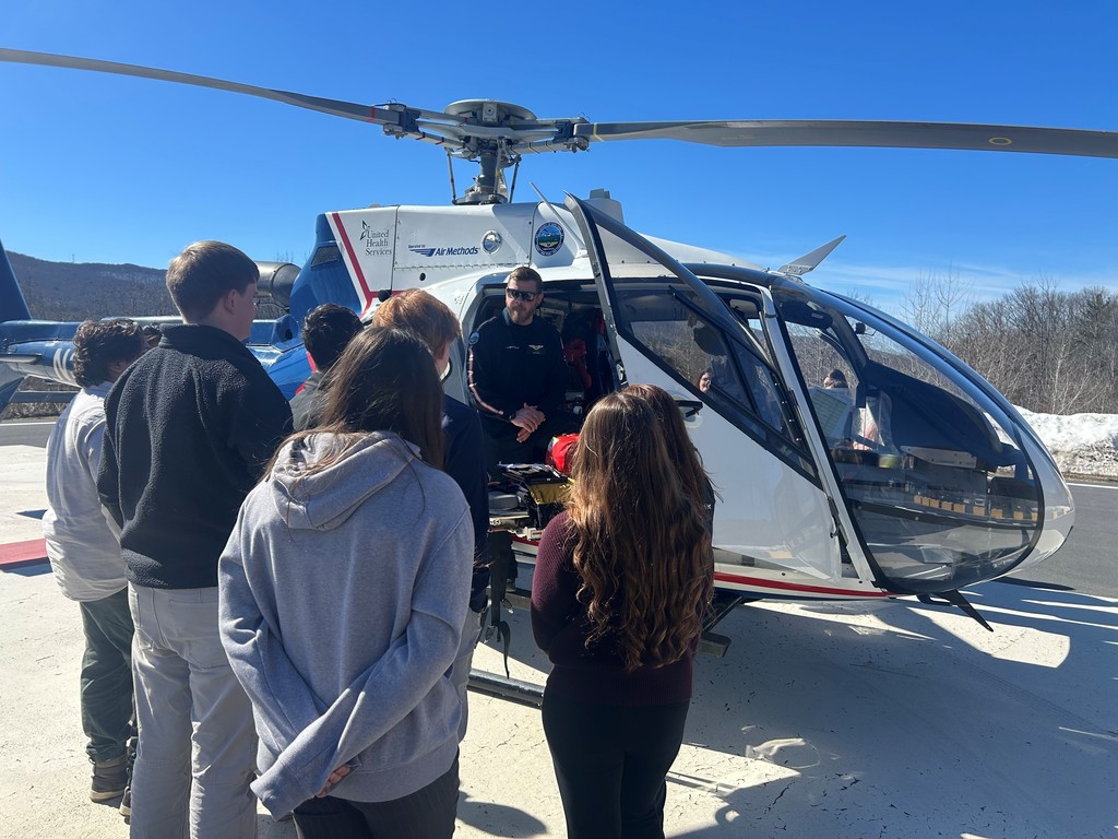Helicopter pilot sitting in the helicopter with the doors open speaking to students