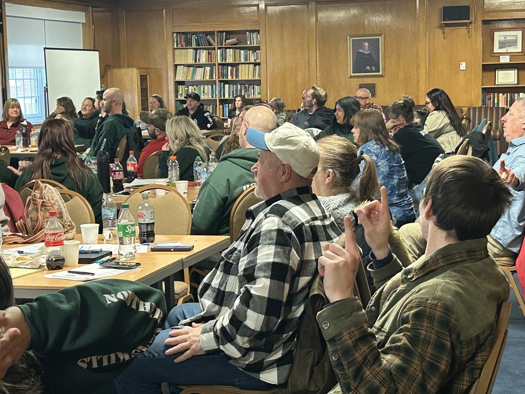 Staff and faculty sitting at tables listening to a presentation.