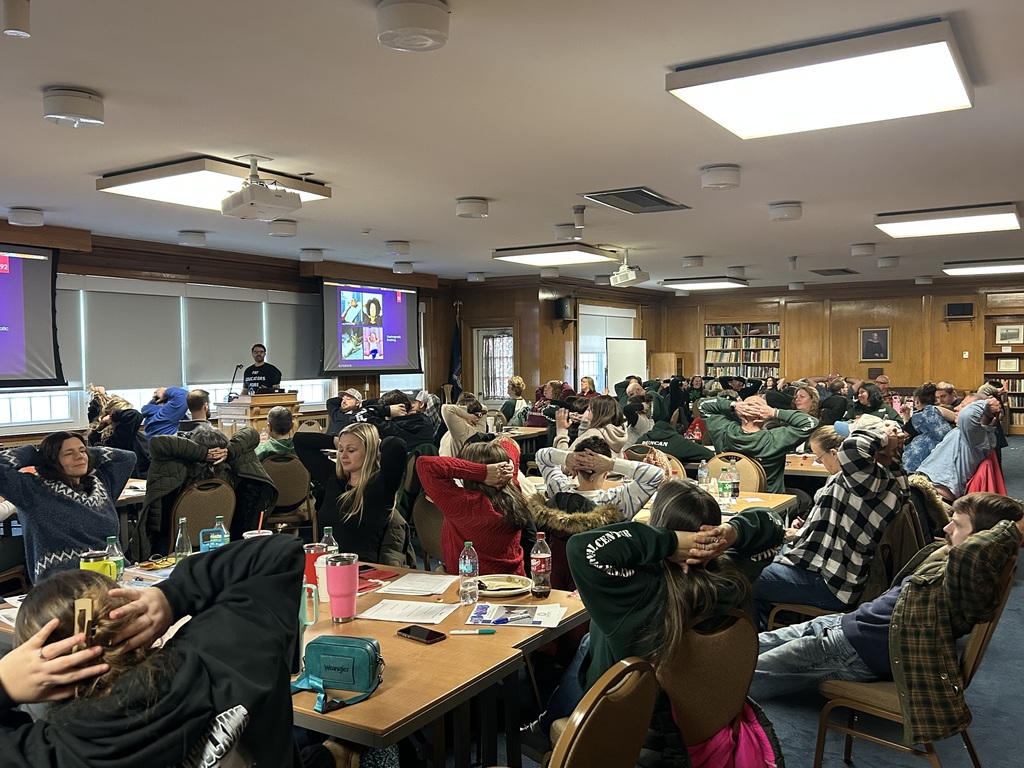 Staff and faculty sitting at tables listening to a presentation.