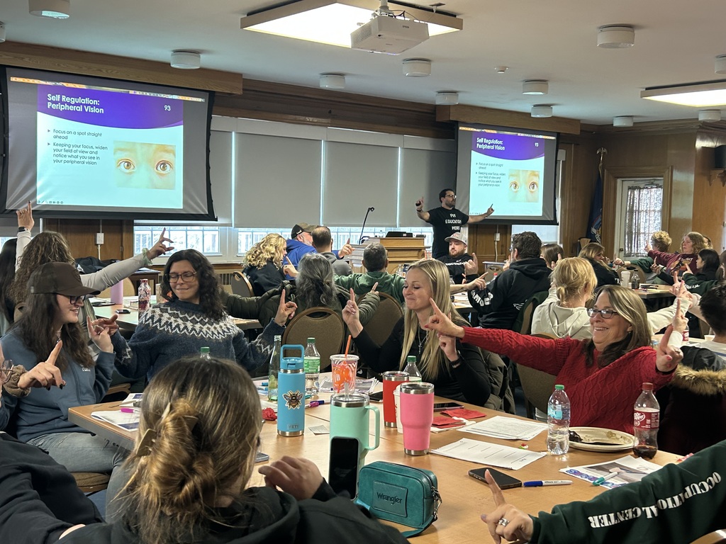 Staff and faculty sitting at tables listening to a presentation.