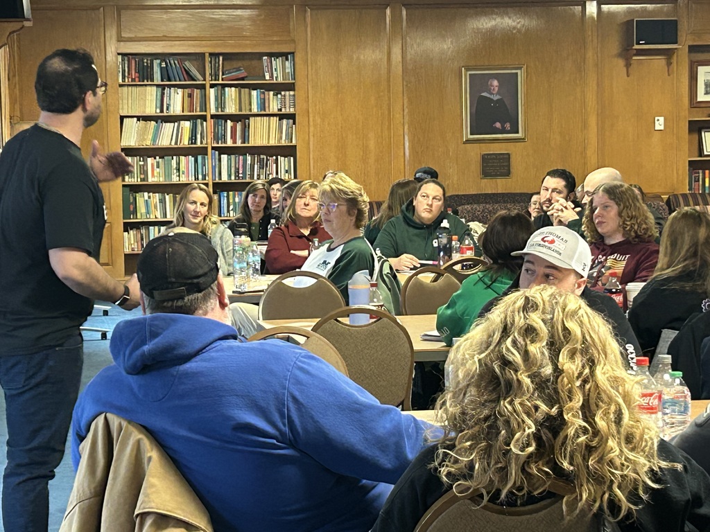 Staff and faculty sitting at tables listening to a presentation.