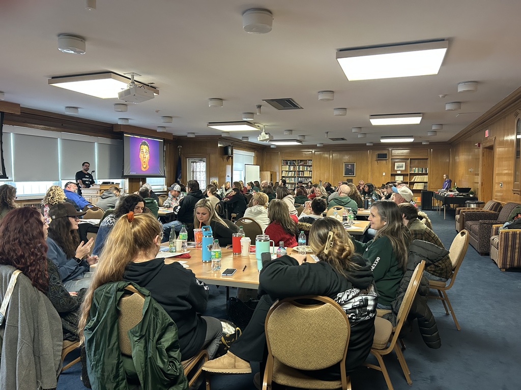 Staff and faculty sitting at tables listening to a presentation.