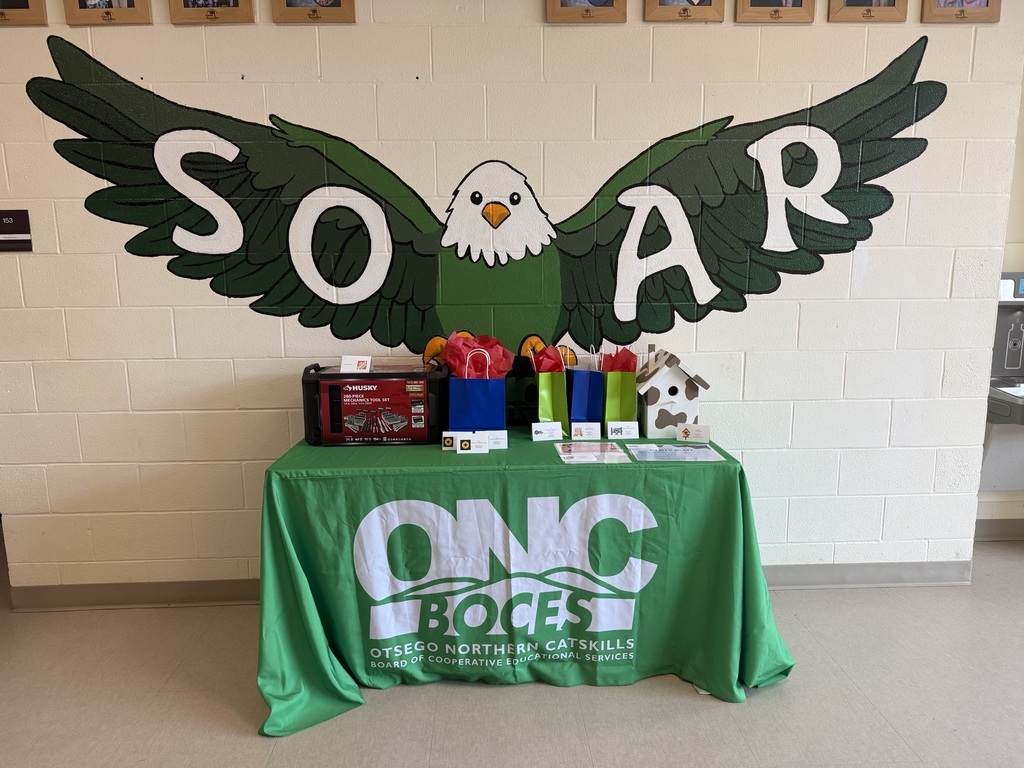 Table with door prizes on a table with an ONC BOCES tablecloth in front of a painted eagle with SOAR written on the wings