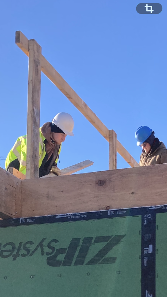 A student is on top of the building with wood and another worker.