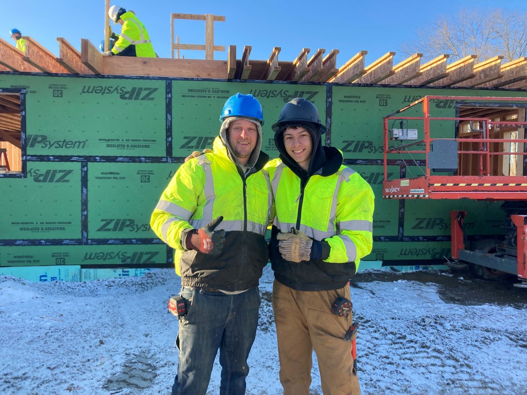 Student posing with a worker in front of the building being constructed.