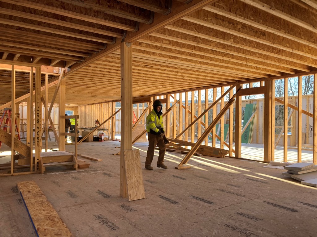 Student inside the building being built walking on plywood. The building has been woodframed.