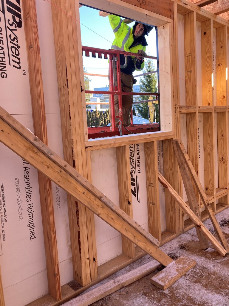 A student on the outside of the unfinished building. He is on a lift working on the outside of the building near a hole where a window will be.