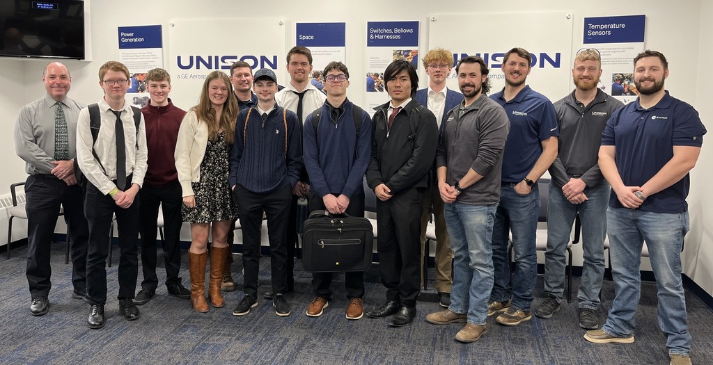 8 students, the class instructor, and 5 employees of Unison pose for a picture in front of Unison signs and information