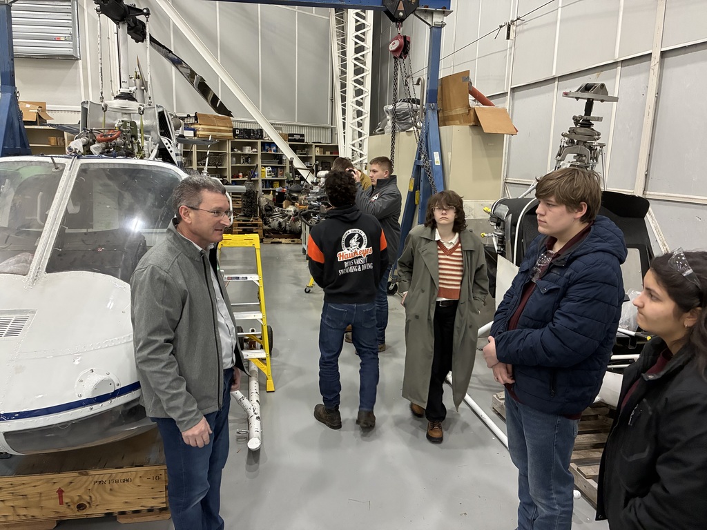 6 students along with one employee in a shop. There is a mock cockpit in the shop.