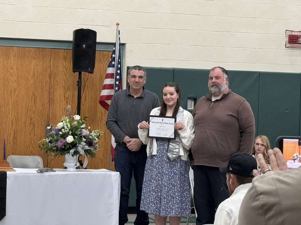 Two instructors and a student holding a certificate are standing near a table with flowers with the American flag behind them.