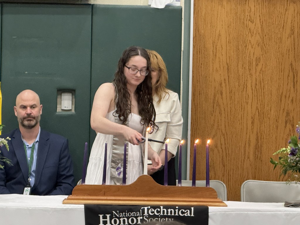 A student lighting a candle representing the pillars of NTHS. Two staff members are in the background.