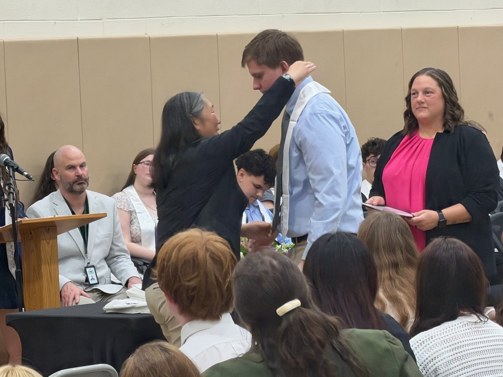 instructor placing honor stole on student. Building principal is standing to the side waiting to give the student their certificate.
