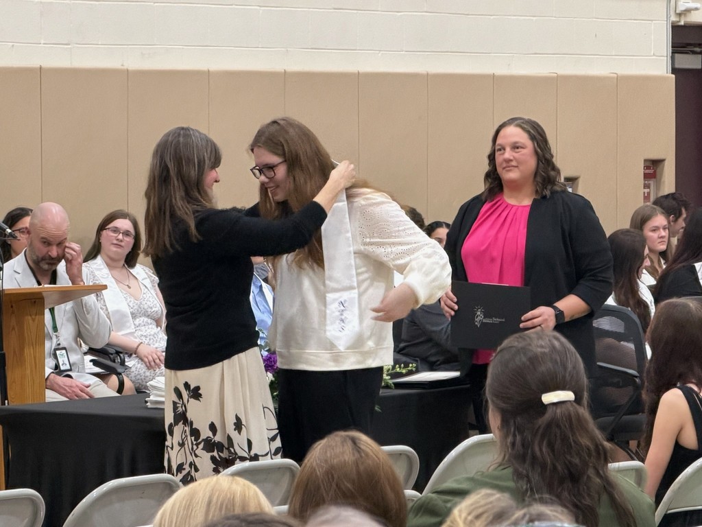 instructor placing honor stole on student. Building principal is standing to the side waiting to give the student their certificate.