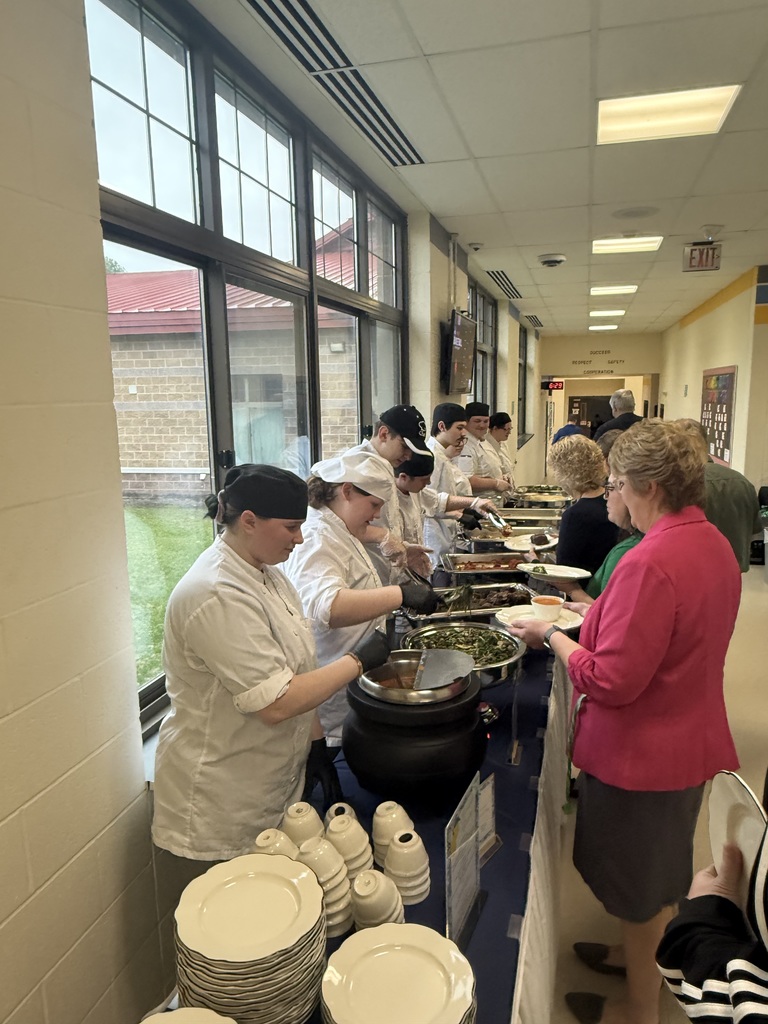 Culinary students serving food in a buffet line with attendees standing with plates waiting to be served
