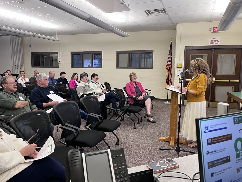 Board president speaking at a podium with people in the audience sitting in chairs 